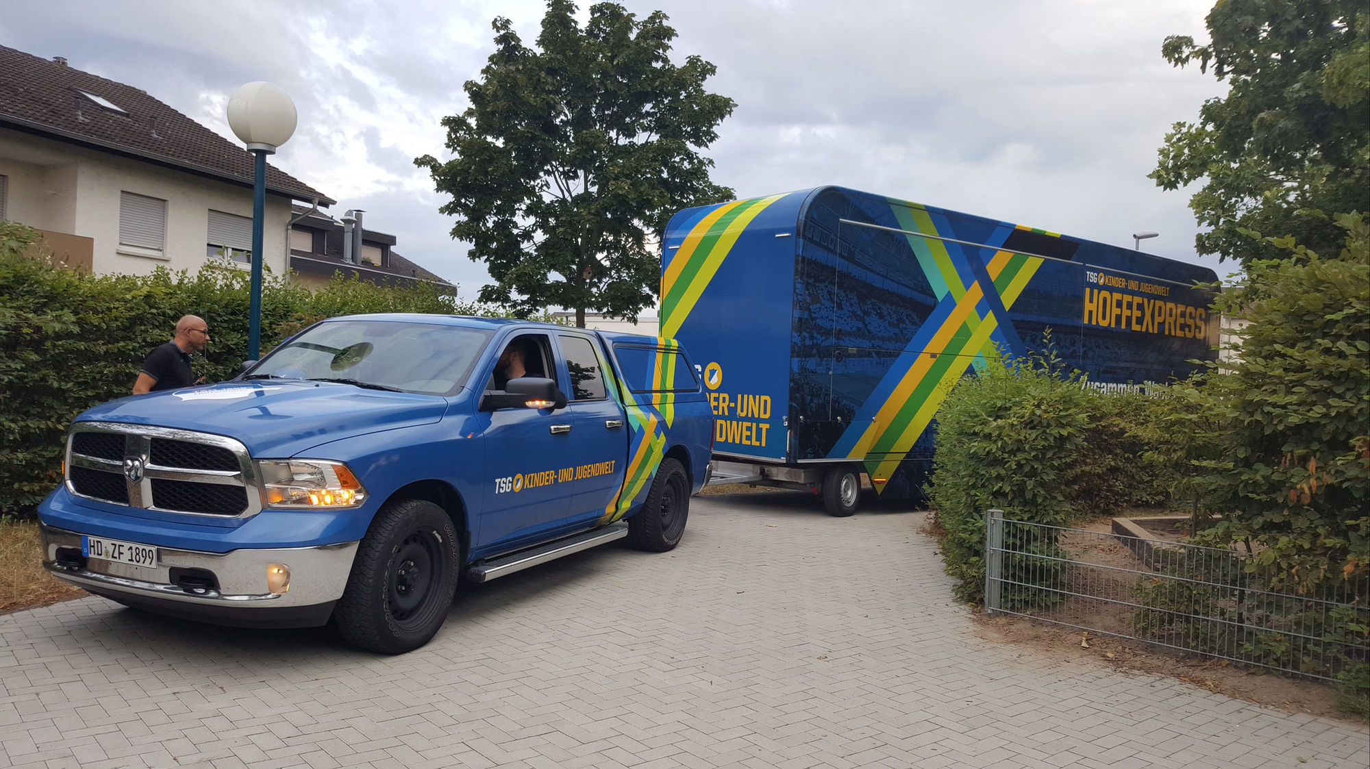 Ein blauer Last Wagen mit einem großen Anhänger steht vor einem Haus