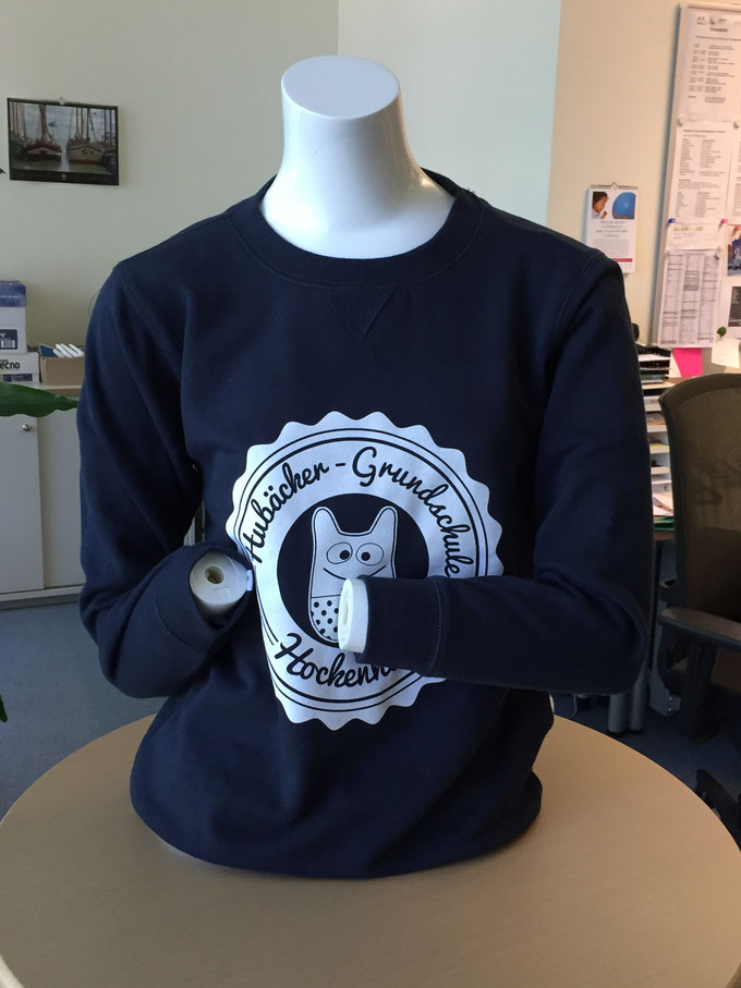 Ein weißer Puppen Körper trägt einen dunklen Pullover mit Hubs Logo in einem Raum